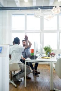 Two male graphic designers giving high five to each other in office
